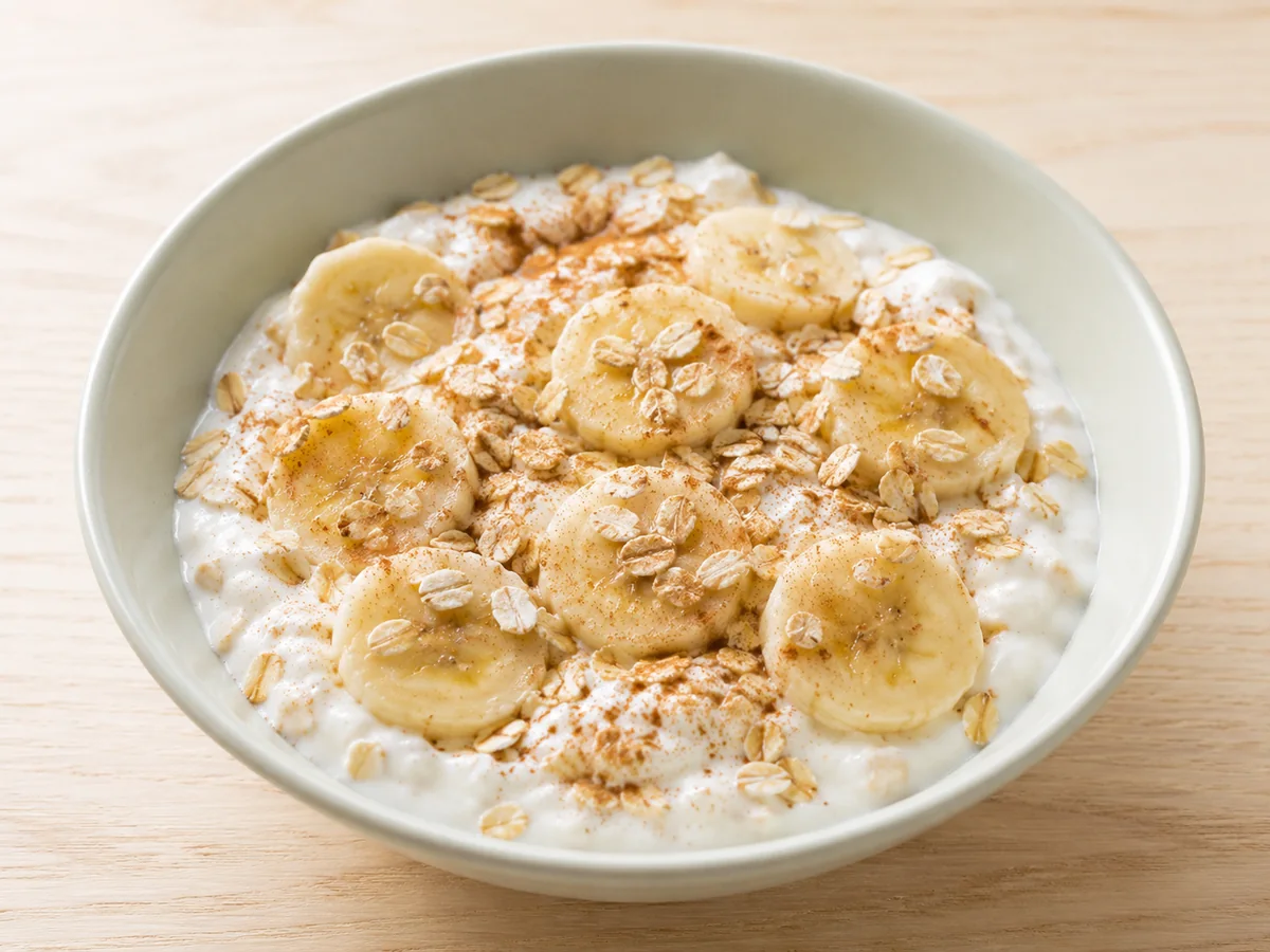 Iogurte natural com rodelas de banana, aveia e canela em tigela clara